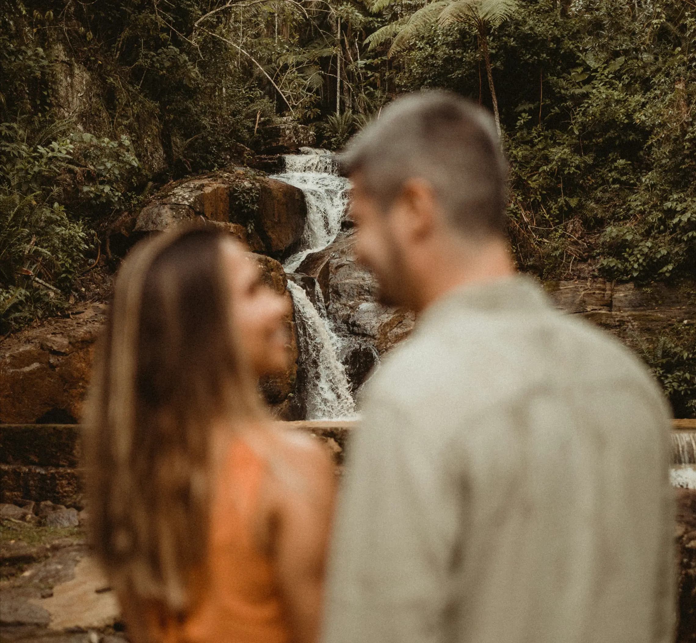 Cachoeira em foco com casal desfocado à frente da cachoeira